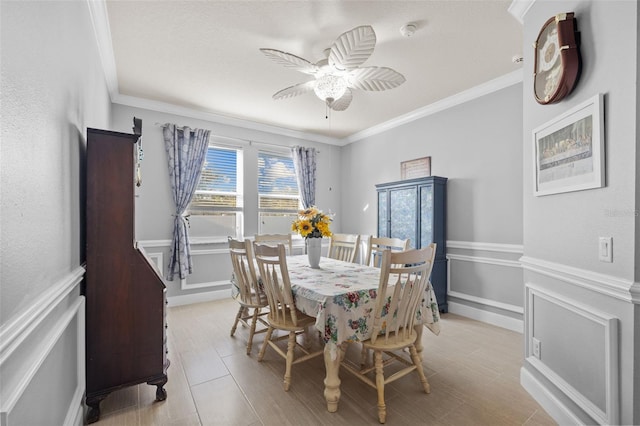 dining area with a decorative wall, wainscoting, a ceiling fan, and crown molding