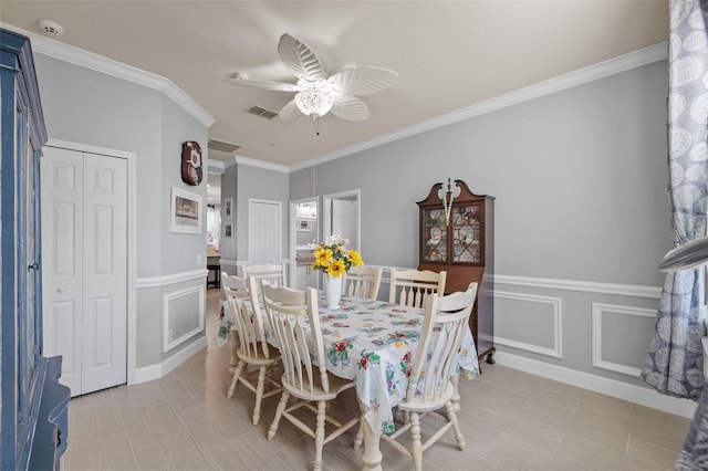 dining room with visible vents, ceiling fan, a wainscoted wall, ornamental molding, and a decorative wall