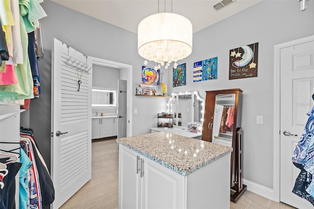 kitchen featuring light stone countertops, visible vents, a kitchen island, white cabinets, and pendant lighting