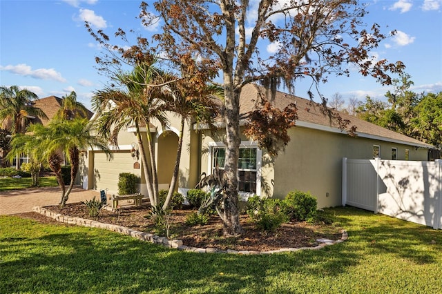 view of front of home featuring a front lawn, fence, stucco siding, a garage, and driveway