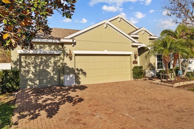 ranch-style home with decorative driveway, a garage, and stucco siding