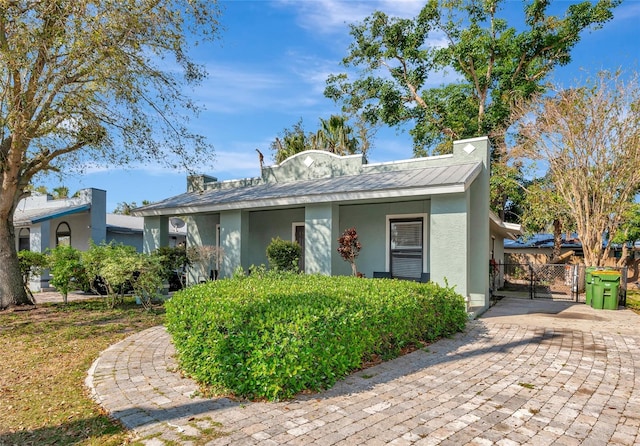 view of front of home featuring stucco siding, fence, metal roof, and a gate