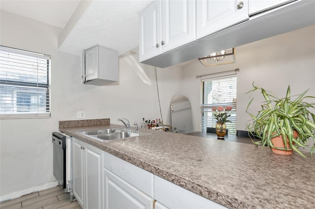 kitchen with dishwashing machine, baseboards, a sink, white cabinets, and light wood-style floors