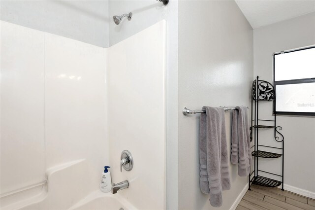 bathroom with tub / shower combination, baseboards, and wood finished floors