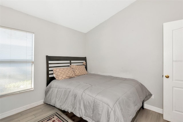 bedroom featuring baseboards, wood finished floors, and vaulted ceiling