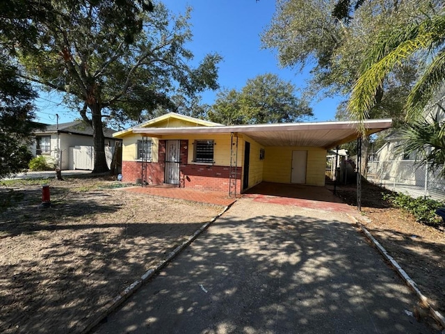 view of front of home with brick siding, an attached carport, aphalt driveway, and fence