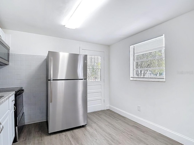 3512 N 10th St, Tampa, FL 33605 - kitchen with black electric range, light countertops, light wood-style flooring, white cabinetry, and freestanding refrigerator