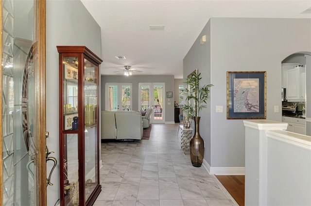 hallway featuring visible vents, arched walkways, marble finish floor, and baseboards