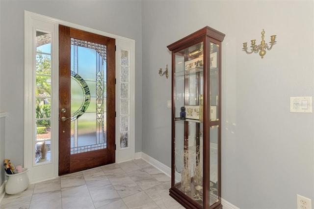 foyer entrance with a wealth of natural light, marble finish floor, and baseboards