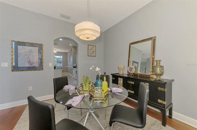 dining room featuring wood finished floors, arched walkways, visible vents, and baseboards