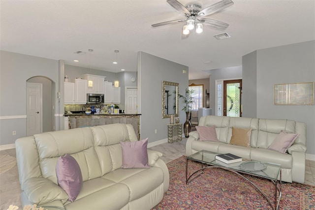 living area featuring arched walkways, visible vents, baseboards, and a ceiling fan