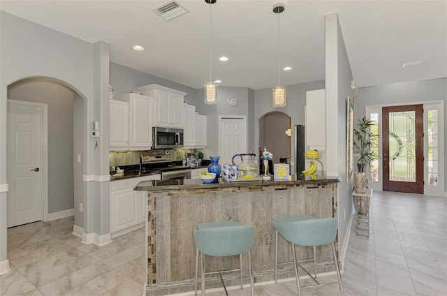 kitchen featuring visible vents, a kitchen bar, arched walkways, appliances with stainless steel finishes, and white cabinets