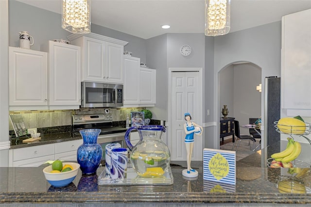 kitchen with dark stone countertops, arched walkways, appliances with stainless steel finishes, and white cabinetry