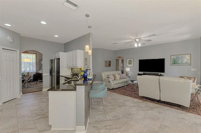 kitchen featuring visible vents, arched walkways, freestanding refrigerator, a sink, and white cabinets