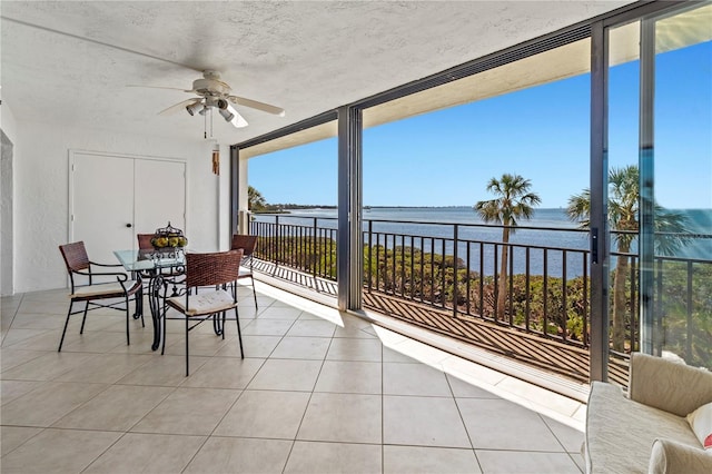 sunroom with a ceiling fan and a water view