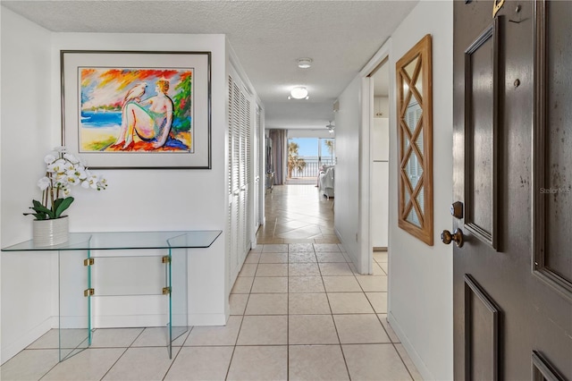 hall featuring baseboards, a textured ceiling, and light tile patterned flooring