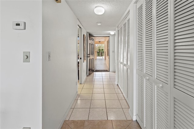 corridor featuring light tile patterned floors, a textured ceiling, and baseboards