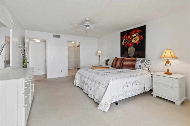 bedroom with a ceiling fan, visible vents, a textured ceiling, light carpet, and connected bathroom