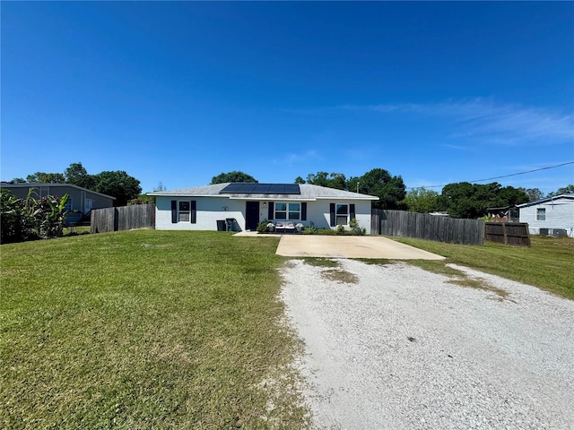 ranch-style house featuring roof mounted solar panels, driveway, a front lawn, and fence