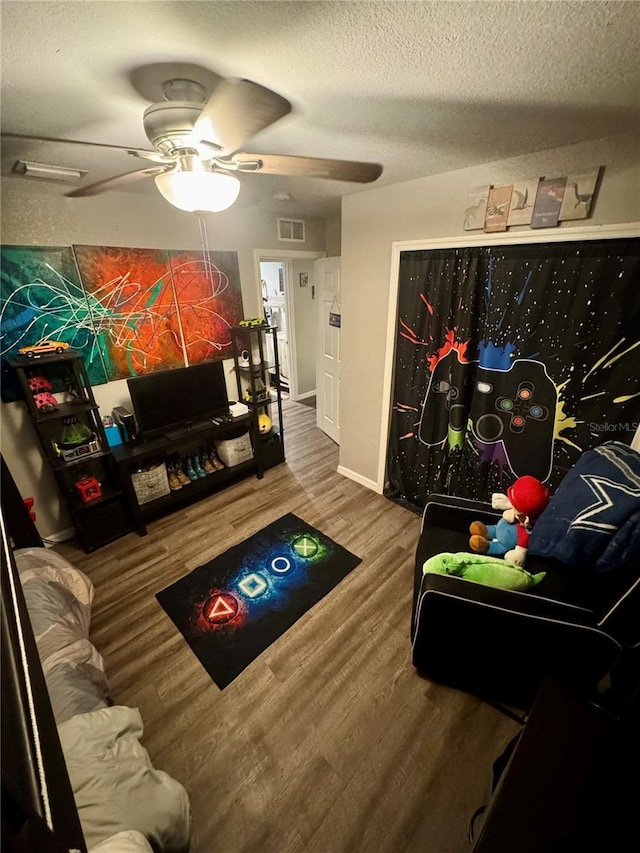 rec room with a ceiling fan, baseboards, wood finished floors, visible vents, and a textured ceiling