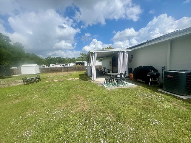 view of yard featuring an outbuilding, fence, a storage shed, central air condition unit, and a patio area