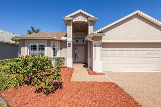 ranch-style home featuring decorative driveway, an attached garage, and stucco siding