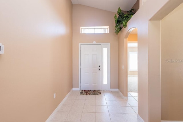 entrance foyer featuring arched walkways, light tile patterned floors, high vaulted ceiling, and baseboards