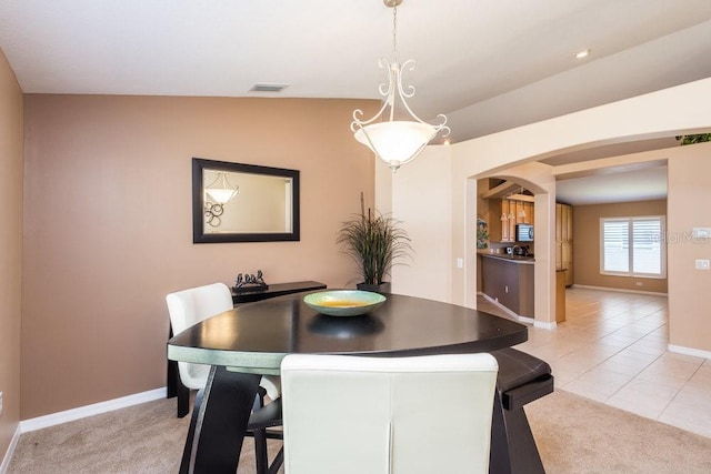 dining space featuring light tile patterned floors, baseboards, arched walkways, and light carpet