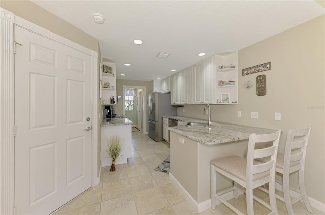 kitchen featuring open shelves, light stone countertops, freestanding refrigerator, and a sink