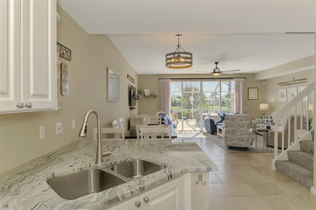 kitchen featuring light stone countertops, light tile patterned flooring, ceiling fan, a sink, and open floor plan