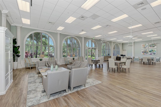 living area with ornate columns, crown molding, visible vents, and light wood finished floors