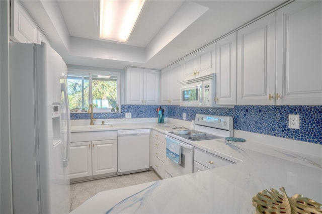 kitchen with a sink, white cabinetry, white appliances, light countertops, and a raised ceiling