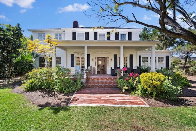 view of front of home featuring a porch, a front lawn, a chimney, and ceiling fan