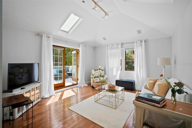 living area with lofted ceiling with skylight, visible vents, track lighting, and hardwood / wood-style flooring