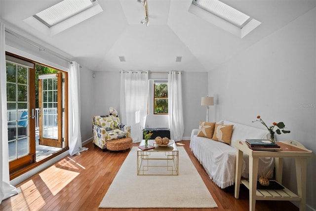 living room with hardwood / wood-style floors, vaulted ceiling with skylight, visible vents, and baseboards