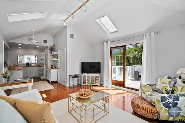 living area featuring a ceiling fan, lofted ceiling with skylight, wood finished floors, and visible vents