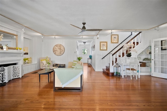 living area with stairs, wood finished floors, a fireplace, and ceiling fan