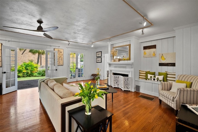 living room with a ceiling fan, wood finished floors, a fireplace, track lighting, and crown molding