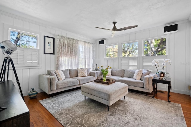 living room with a ceiling fan, a decorative wall, wood finished floors, and baseboards