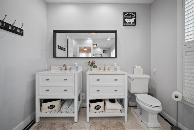 bathroom with a sink, baseboards, toilet, and two vanities