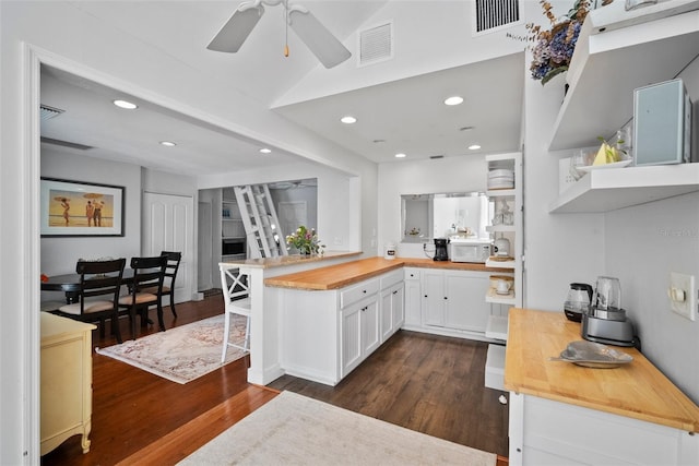 kitchen featuring white microwave, visible vents, a peninsula, wood counters, and open shelves