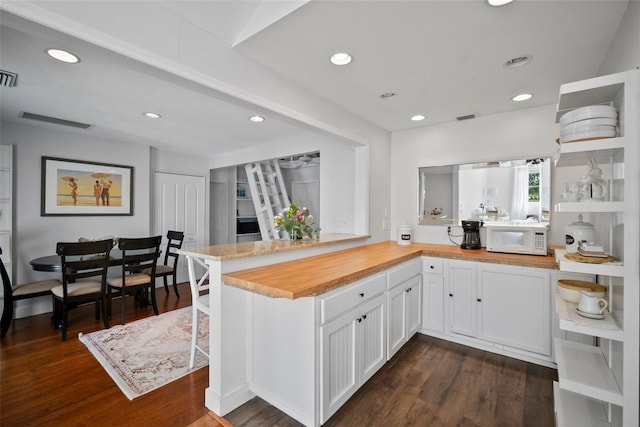 kitchen featuring dark wood-style floors, white microwave, a peninsula, wood counters, and white cabinetry