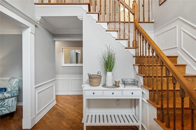 staircase with a decorative wall, wood finished floors, and ornamental molding