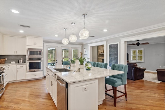 kitchen featuring a kitchen bar, appliances with stainless steel finishes, light wood-style floors, white cabinets, and a sink