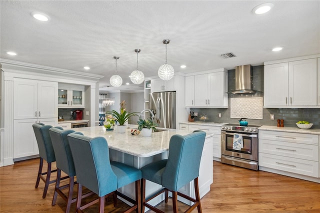 kitchen with a kitchen breakfast bar, wall chimney range hood, white cabinets, and appliances with stainless steel finishes