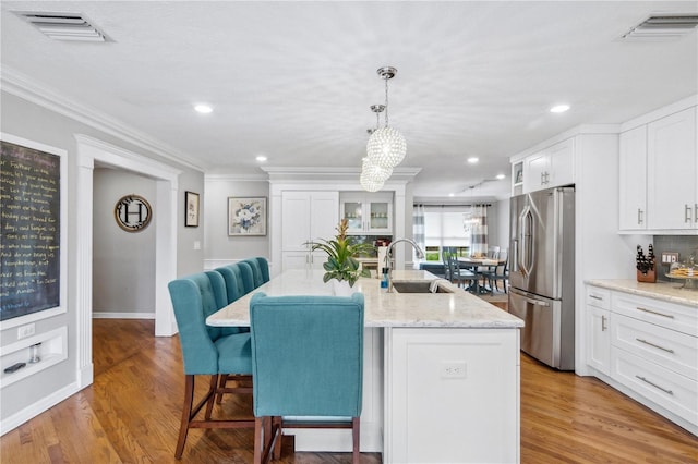 kitchen featuring a breakfast bar, visible vents, freestanding refrigerator, and a sink