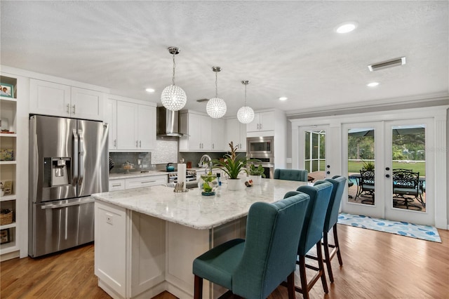 kitchen featuring visible vents, appliances with stainless steel finishes, wood finished floors, white cabinets, and wall chimney exhaust hood