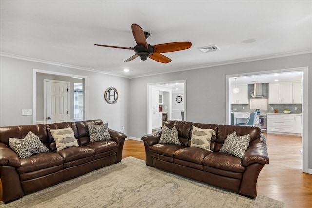 living area featuring light wood finished floors, visible vents, a ceiling fan, and ornamental molding