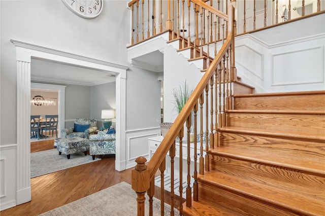 stairway with a notable chandelier, ornamental molding, a decorative wall, and wood finished floors