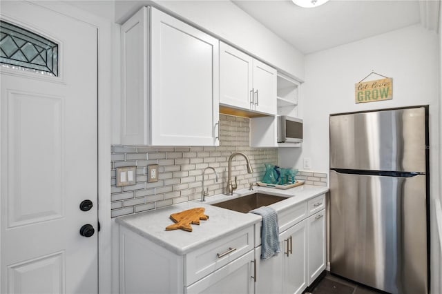 kitchen with a sink, open shelves, tasteful backsplash, freestanding refrigerator, and white cabinets